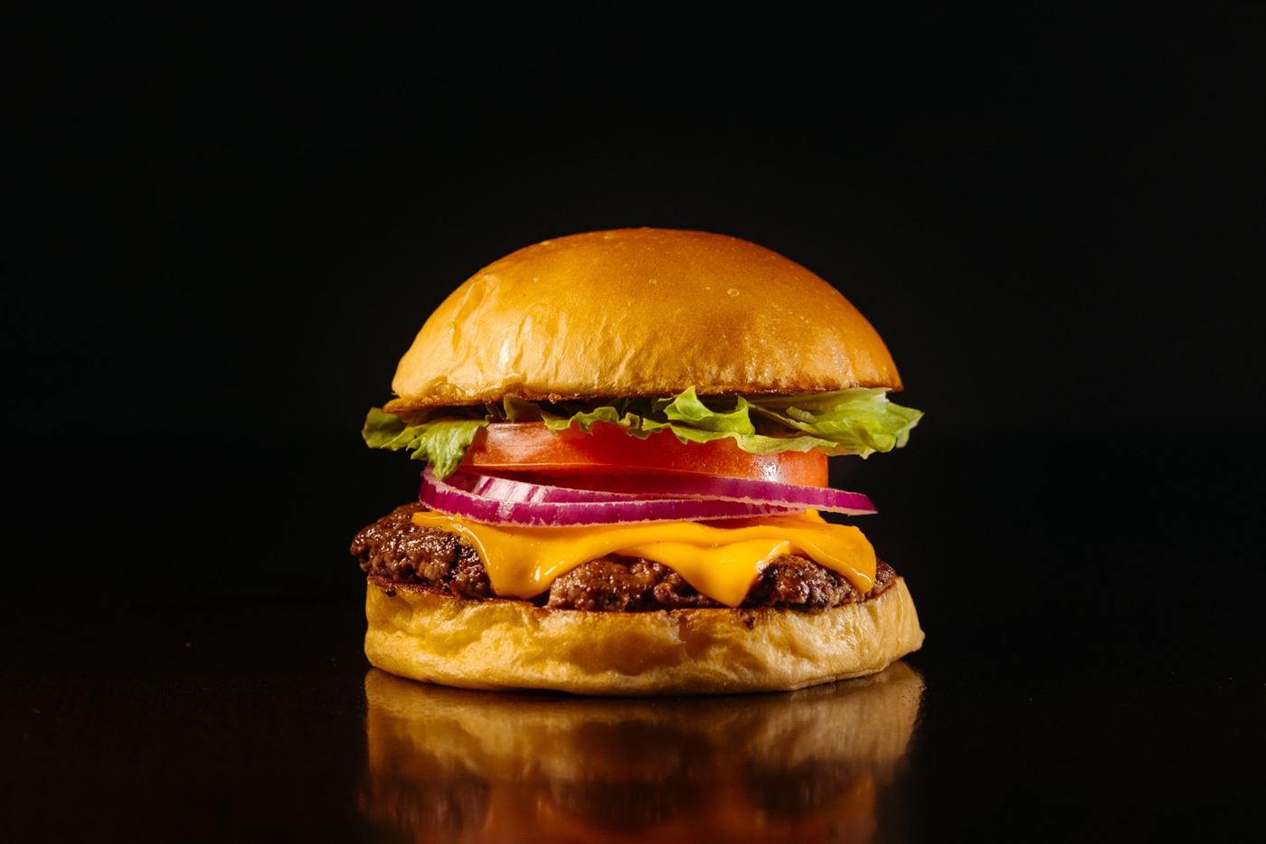 Cheeseburger com alface, tomate e cebola roxa sobre fundo preto