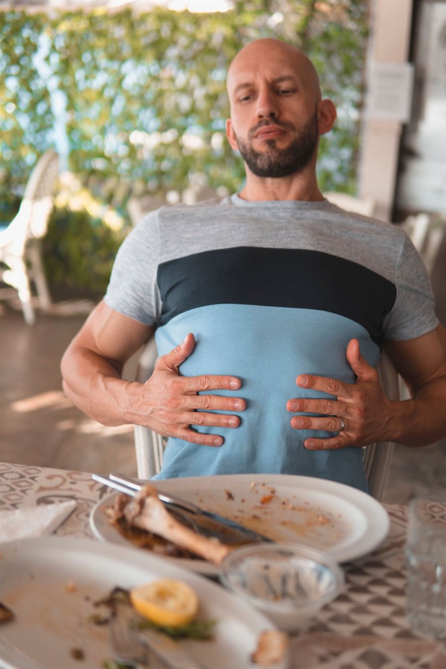 Homem sentado à mesa depois do almoço, com as mãos na barriga, olhando os pratos vazios