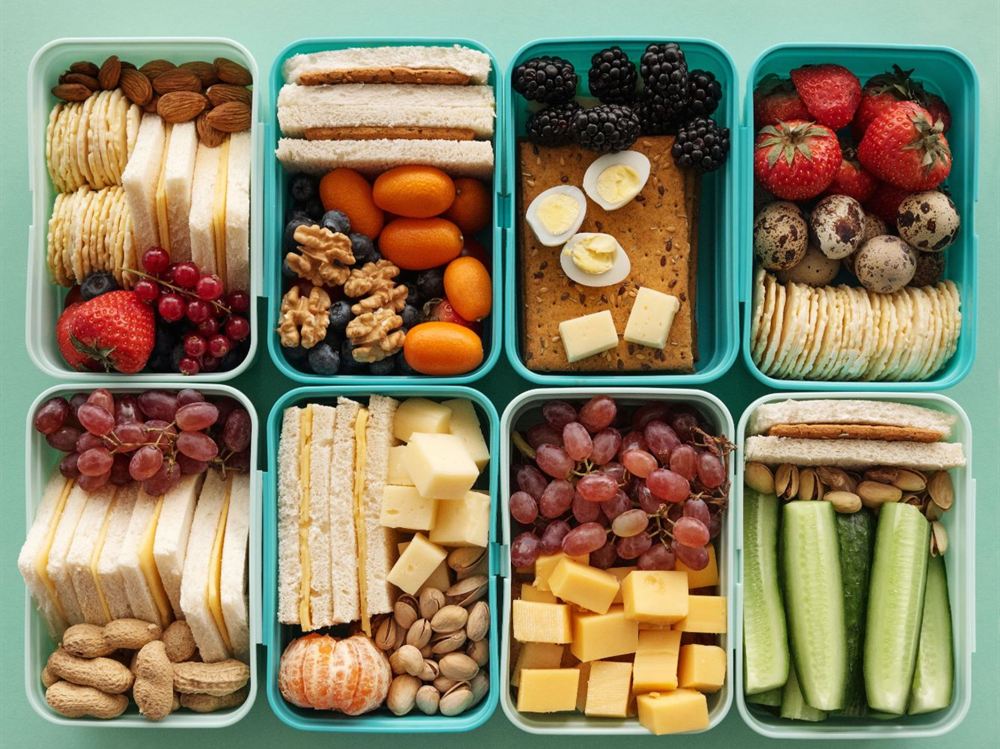 Oito potes de lanche com frutas, castanhas, sanduíches, queijo e pepino, vistos de cima
