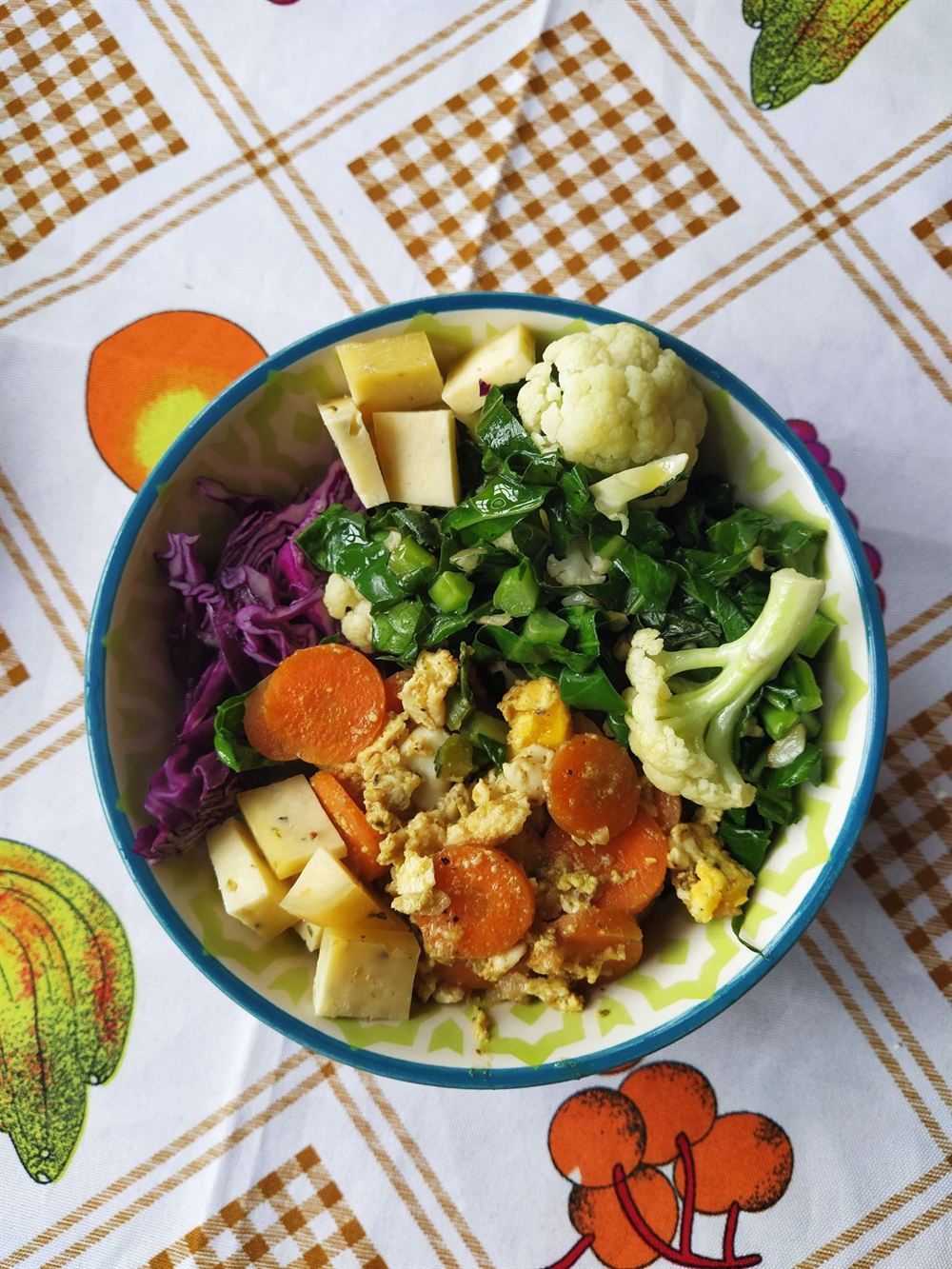 Tigela com couve, couve-flor, cenoura, repolho roxo, queijo e ovo sobre toalha de frutas